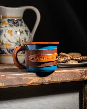 Camping mug 330ml with blue enamel finish and leather sleeve for outdoor adventures, straight front view