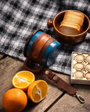 Blue enamel camping mug with handcrafted leather wrap and brass hardware, overhead view showing base detail