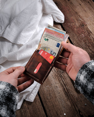 Dogaart Athen Minimal Card Holder Brown Waxed pull up leather cüzdan iki elde tutuluyor ve banknotlar ön planda, çok sayıda ban...
