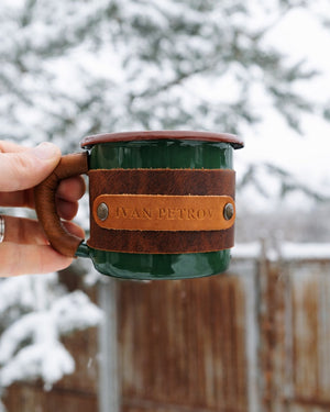 Green leather-wrapped enamel mug held comfortably in hand demonstrating ergonomic grip and portable design