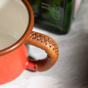 Outdoor gear enamel mug with leather wrapped handle, premium stitching craftsmanship, close-up detail