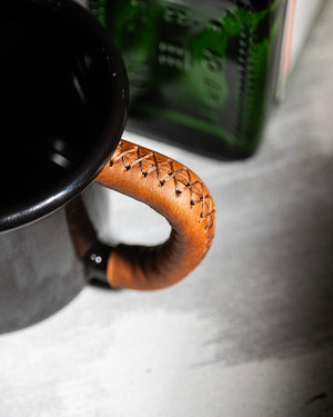 Camping mug handle wrapped in handcrafted leather with precise stitching detail, close-up view