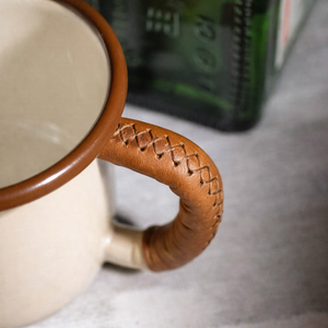 Handcrafted leather handle wrap on enamel hiking mug showing detailed stitching, close-up view