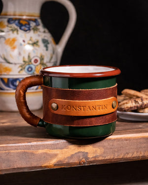 Side profile view highlighting leather-wrapped handle design on green enamel mug with artisan craftsmanship details