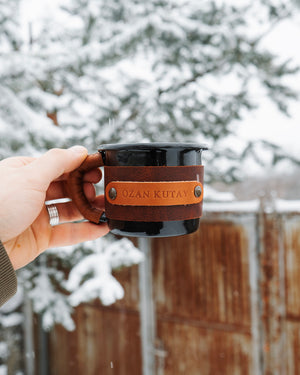 Handcrafted leather enamel mug designed for outdoor use, comfortable grip demonstration in hand