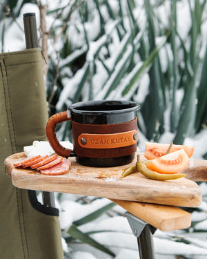 Travel mug with leather sleeve perfect for camping and hiking, outdoor setting front view
